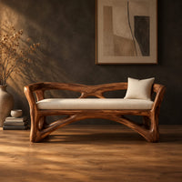 Bench with a sculpted open wooden frame, low arms and a pale cushion in a dark studio against a charcoal plaster wall
