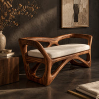Corner detail of bench with a sculpted open wooden frame, low arms and a pale cushion beside wood, brass and linen samples