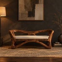 Bench with a sculpted open wooden frame, low arms and a pale cushion in a dark entryway at golden hour