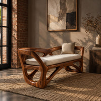 Bench with a sculpted open wooden frame, low arms and a pale cushion in an industrial loft entryway with exposed brick