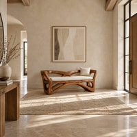 Bench with a sculpted open wooden frame, low arms and a pale cushion in a bright open plan entryway