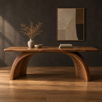 Desk with a slab top on two arched legs and a half moon notch in a dark studio against a charcoal plaster wall