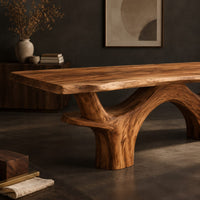 Corner detail of live edge dining table with arching branch legs under a slab top beside wood, brass and linen samples