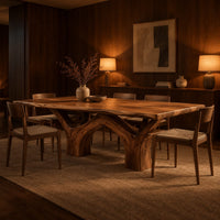 Live edge dining table with arching branch legs under a slab top in an evening dining room with walnut wall paneling