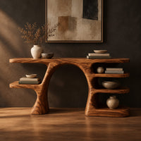 Arched console table with a branch shaped leg and stacked oval shelves in a dark studio against a charcoal plaster wall