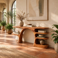 Arched console table with a branch shaped leg and stacked oval shelves in a bright entryway with arched windows and plants