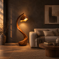 Floor lamp with a long arching wooden stem and a carved hood shade in a dark living room at golden hour