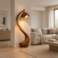 Floor lamp with a long arching wooden stem and a carved hood shade in a Scandinavian living room with white walls