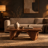 Thick slab coffee table on carved arch legs with circular cutouts in a dark living room at golden hour