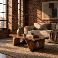 Thick slab coffee table on carved arch legs with circular cutouts in an industrial loft living room with exposed brick