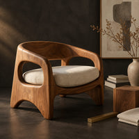 Corner detail of low barrel back chair with oval side openings and arched legs beside wood, brass and linen samples