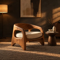 Low barrel back chair with oval side openings and arched legs in a dark living room at golden hour