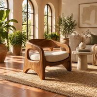 Low barrel back chair with oval side openings and arched legs in a bright living room with arched windows and plants