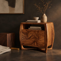 Corner detail of barrel sided nightstand with an open top cubby and a swirled grain front beside wood, brass and linen samples