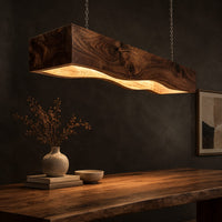 Long beam pendant light with a wavy lower edge and a warm glow, three-quarter view showing the grain