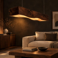 Long beam pendant light with a wavy lower edge and a warm glow in a dark living room at golden hour