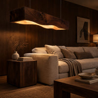 Long beam pendant light with a wavy lower edge and a warm glow in an evening living room with walnut wall paneling