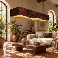 Long beam pendant light with a wavy lower edge and a warm glow in a bright living room with arched windows and plants
