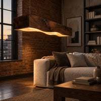 Long beam pendant light with a wavy lower edge and a warm glow in an industrial loft living room with exposed brick