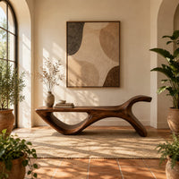 Long flat bench with an open loop base and one raised end in a bright entryway with arched windows and plants