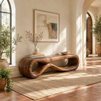 Low wood bench shaped as a figure eight loop with a smooth top in a bright entryway with arched windows and plants
