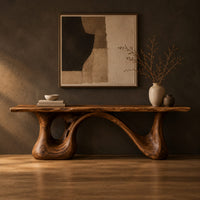 Long low slab bench with a wavy edge on a sculpted base in a dark studio against a charcoal plaster wall