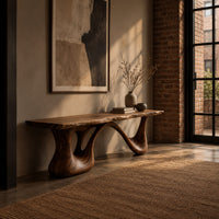 Long low slab bench with a wavy edge on a sculpted base in an industrial loft entryway with exposed brick