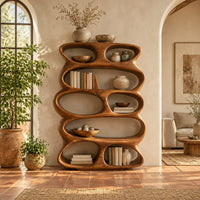 Tall sculpted bookshelf with stacked oval openings of mixed sizes in a bright living room with arched windows and plants