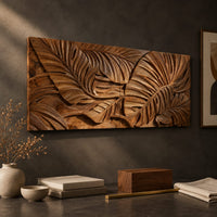 Detail of carved wood wall art panel with overlapping tropical leaves in deep relief beside wood, brass and linen samples