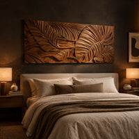 Carved wood wall art panel with overlapping tropical leaves in deep relief above a bed in a dusk lit bedroom