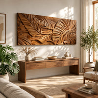 Carved wood wall art panel with overlapping tropical leaves in deep relief in a bright sunroom with green plants