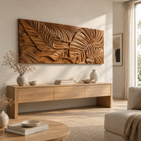 Carved wood wall art panel with overlapping tropical leaves in deep relief above a light oak sideboard in daylight