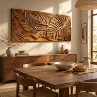 Carved wood wall art panel with overlapping tropical leaves in deep relief beside a dining table in natural light