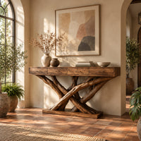 Console table with four slim drawers on a base of crossed tree branches in a bright entryway with arched windows and plants