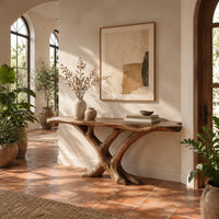Live edge console table with a base of crossed branch shaped legs in a bright entryway with arched windows and plants