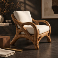 Corner detail of lounge chair with a branch like wooden frame and soft cream cushions beside wood, brass and linen samples