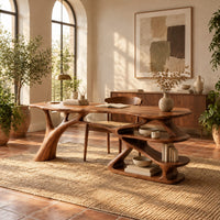 Writing desk with a branch shaped leg and stacked open shelves in a bright home office with arched windows and plants