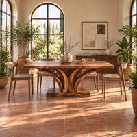 Rectangular dining table with a branching wood pedestal and thick slab top in a bright dining room with arched windows and plants