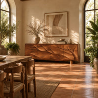 Carved branch sideboard with four flush panels and short cylindrical feet in a bright dining room with arched windows and plants