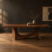 Dining table with a flowing slab top on a branching sculpted base in a dark studio against a charcoal plaster wall