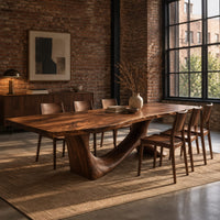 Dining table with a flowing slab top on a branching sculpted base in an industrial loft dining room with exposed brick