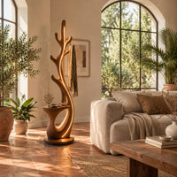 Branching floor lamp with a small shelf and a glowing trunk edge in a bright living room with arched windows and plants