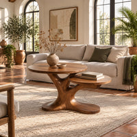 Coffee table with two tops on a branching tree shaped pedestal in a bright living room with arched windows and plants