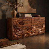 Corner detail of sideboard with a carved breaking wave across the doors beside wood, brass and linen samples