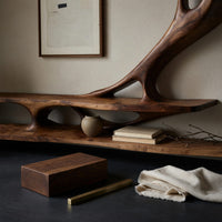 Corner detail of branching wall TV shelf system in carved wood beside wood, brass and linen samples