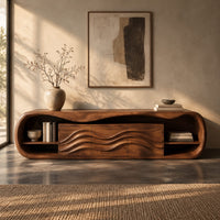 Corner detail of capsule shaped tv stand with open end shelves and wave carved center panels beside wood, brass and linen samples