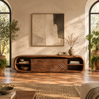 Low capsule shaped wooden tv stand with wave carved panels and open end shelves in a bright living room with arched windows and plants
