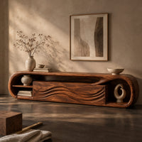 Corner detail of capsule shaped tv stand with wave carved panels and open end shelves beside wood, brass and linen samples