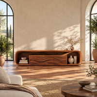 Capsule shaped media console with wave carved center panels and open end cubbies in a bright living room with arched windows and plants