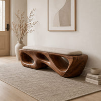 Chunky wooden bench with sculpted cutouts and a slim cream cushion on top in a Scandinavian entryway with white walls